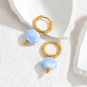 Detail shot of gold shell tassel earrings with light blue pendants on a stone surface