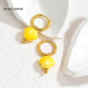 Close-up of golden hoop earrings featuring yellow shell charms with three gold beads