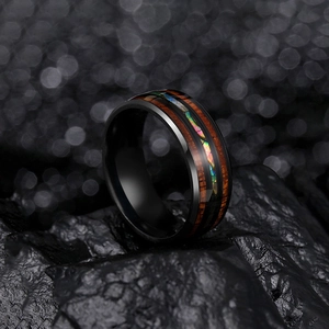 Polished black titanium ring with wood grain and abalone shell inlay on dark rock