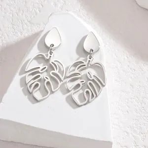 Detailed view of silver stainless steel monstera leaf earrings on a white stone base