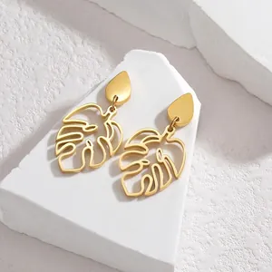 Detail of golden monstera leaf earrings with teardrop studs on a textured stone base
