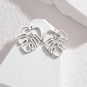 Detailed view of silver hollowed monstera leaf earrings on a white textured background