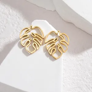 Macro shot of gold hollow monstera leaf earrings on a minimalist white stone pedestal