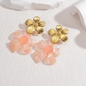 Détail de boucles d'oreilles fleurs avec pétales dorés et pendentifs en résine rose
