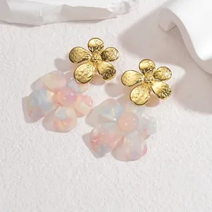 Détail de boucles d'oreilles fleurs en résine avec métal doré martelé et accents de perle
