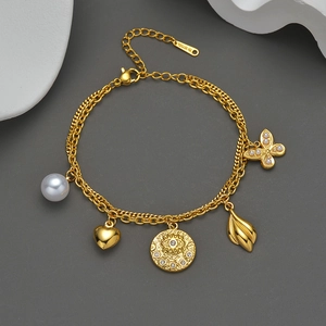 Detail of layered gold stainless steel bracelet with pearl, heart, and evil eye charms