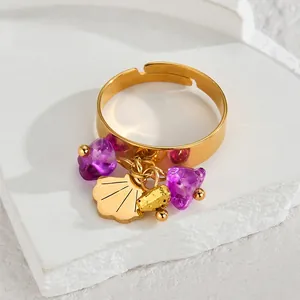 Detailed close-up of golden shell pendant and purple stone charms on a stainless steel ring