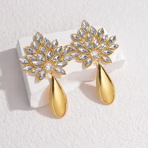 Detailed close-up of 18K gold-plated flower earrings with crystals on a white stone base