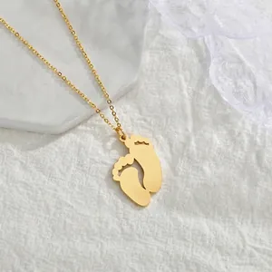 Détail d'un collier pendentif empreinte de bébé doré posé sur un support en pierre blanche