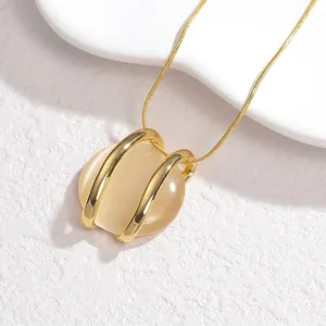 Detail of round beige opal pendant on a gold snake chain necklace against white texture