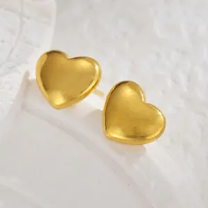 Macro detail of heart-shaped gold studs with a mirror-polished finish on stone backdrop