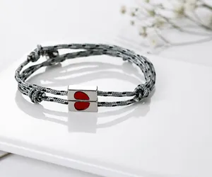 Close-up of woven couple bracelet with silver magnetic half-heart clasp on white surface