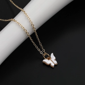 Detailansicht der weißen Schmetterlings-Halskette mit Goldkette auf dunklem Hintergrund