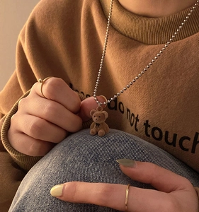 Close-up of a brown flocked teddy bear pendant with silver bead chain and bow detail
