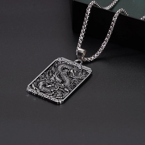 Detail of vintage embossed dragon pattern on square stainless steel pendant with bead chain