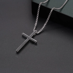 Macro detail of silver box chain and black inlaid cross pendant on a textured surface