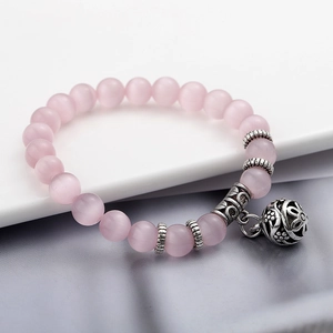 Dettaglio del bracciale con perle occhio di gatto rosa e ciondolo a campana floreale retrò