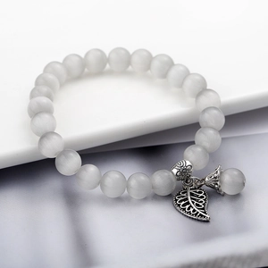 Dettaglio del bracciale con perle occhio di gatto e ciondolo a foglia d'argento su bianco