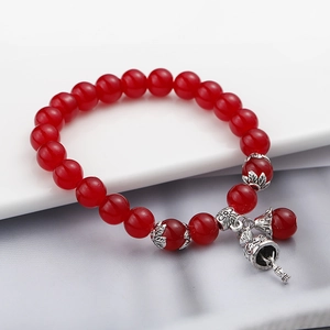 Dettaglio del bracciale di perle occhio di gatto rosse con ciondoli a loto e campanello