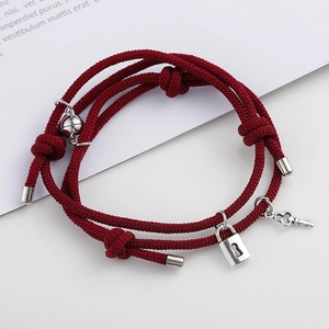 Détail de bracelets de couple tressés rouges avec breloques serrure, clé et perles aimantées