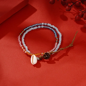 Detailed close-up of Bohemian beaded bracelet with white shell charm on red background