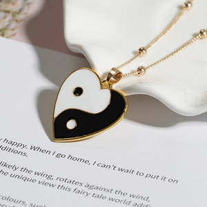 Dettaglio di un ciondolo yin yang a forma di cuore con catena a sfere dorate su bianco