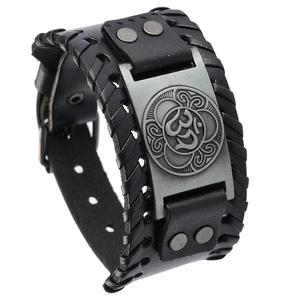 Détail d'un large bracelet en cuir noir avec une plaque en métal gravée du symbole Om vintage