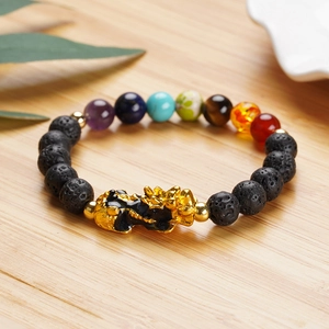 Lava stone chakra bracelet featuring a golden Pixiu charm on a light wooden surface
