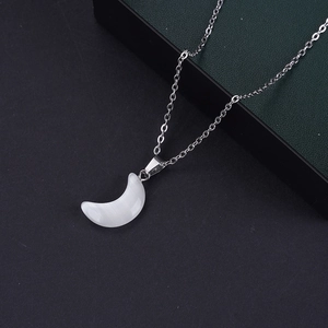 Detalle de un colgante de luna blanca con cadena de plata sobre un fondo negro texturizado