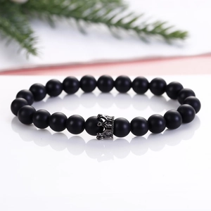 Close-up of matte black agate beads with a detailed crown charm on a reflective surface