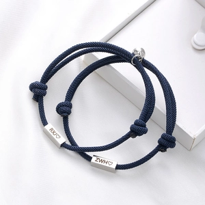 Detail of dark blue braided couple bracelets with custom engraved metal tags and magnetic ball