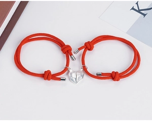 Close-up of red braided couple bracelets with magnetic heart-shaped charms and silver tips