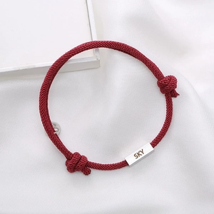 Detail of red woven rope bracelet with engraved SKY silver plate and magnetic buckle