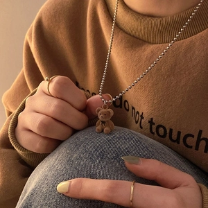 Plush teddy bear pendant necklace with minimalist gold rings on a cozy sweater