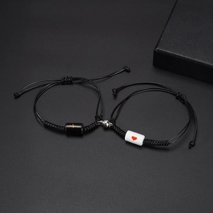 Magnetic braided couple bracelets with heart and heartbeat charms on a dark textured background