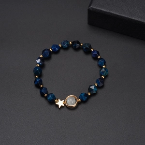 Blue faceted bead bracelet with golden star and moon charms on a black background