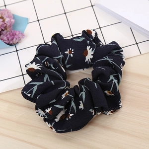 Detailed view of floral dark blue chiffon scrunchie with white daisy pattern on wood