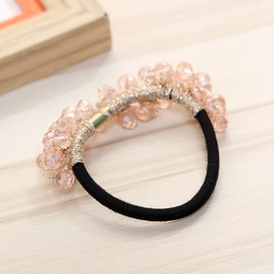 Elastic hair tie with pink crystal beads and gold wire on a light wood background