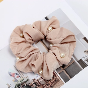 Detailed macro view of champagne satin scrunchie featuring elegant white pearl accents