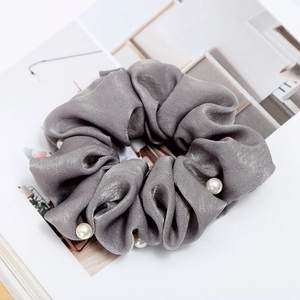 Detailed view of dark grey satin scrunchie with embedded white pearls on magazine background