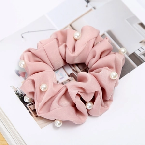 Detailed view of pink satin scrunchie featuring elegant white pearl embellishments