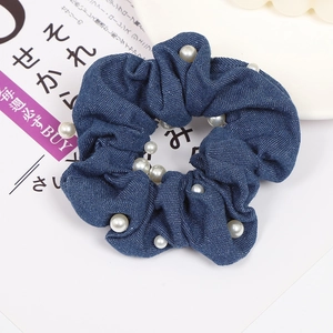 Detailed macro view of dark blue denim fabric scrunchie with elegant white pearl accents