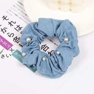 Detailed close-up of light blue denim fabric scrunchie with white pearl embellishments