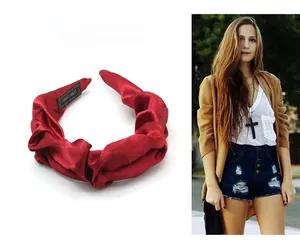 Detail of red pleated satin headband showing handmade label and silky fabric texture