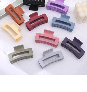 Flat lay of ten colorful matte rectangular hair claws on a textured white background