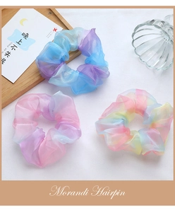 Drei pastellfarbene Organza-Haargummis mit Farbverlauf auf einem Holztablett Deko