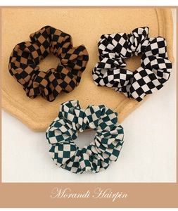 Close-up of three checkered fabric scrunchies in Morandi tones on a ceramic tray