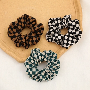 Three checkered checkerboard scrunchies in brown, black, and green on a ceramic tray