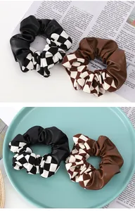 Detail of checkerboard and PU leather patchwork hair scrunchies on a ceramic plate