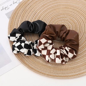 Checkered patchwork hair scrunchies with leather texture on a woven mat display